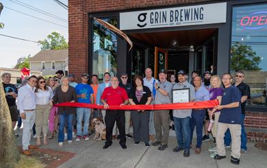 Director Arnone with the owners of Grin Brewing and others, standing in front of the building holding a red ribbon and Proclamation